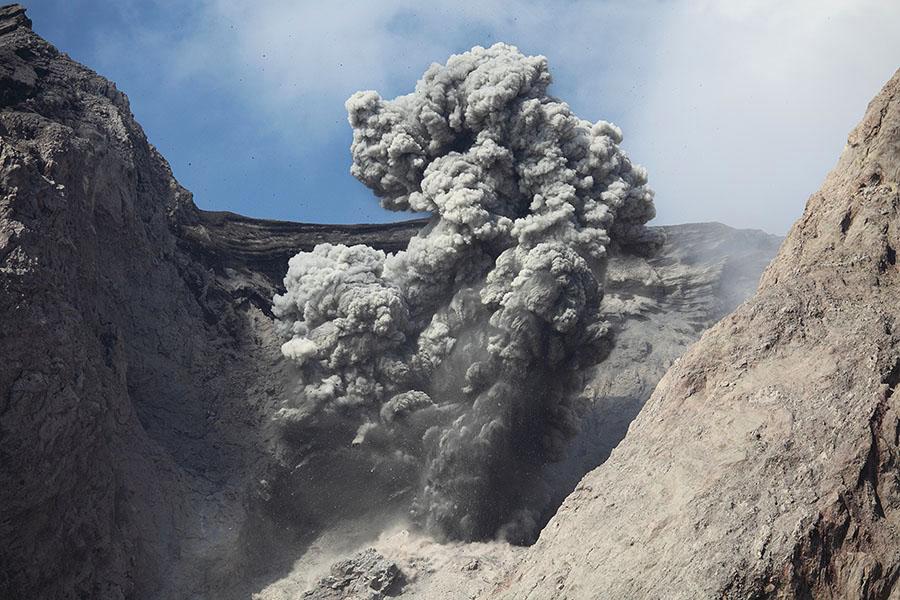 Dark grey ash cloud containing volcanic bombs from powerful ash-rich strombolian eruption of Batu Tara Volcano