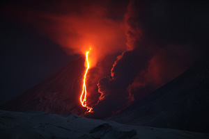 Night eruption of Kliuchevskoi volcano, Kamchatka. Also known as Klyuchevskoy or Klyuchevskaya Sopka. Volcano erupts lava and steam rises as lava flow melts glacier.