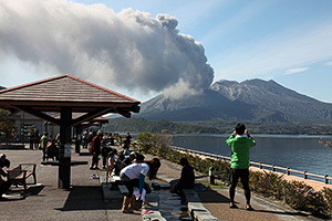 Sakurajima volcano erupting viewed from traditional thermal foot bath
